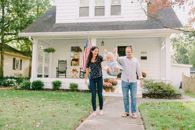 A young family laughing together in front of their first home